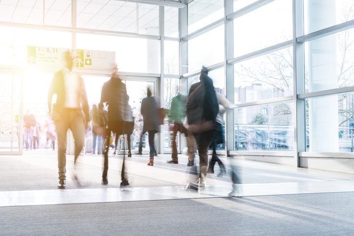 Messebesucher laufen durch eine tageslichthellen Messehalle mit Fensterfront